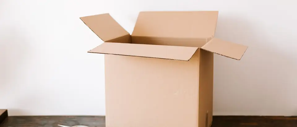 An open cardboard box on an old timber bench beside a roll of tape and scissors