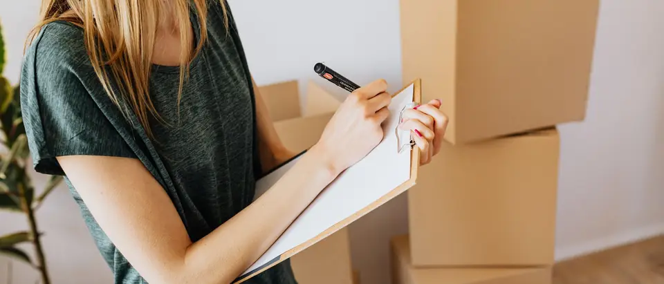 A clipboard list being ticked off beside stacked moving boxes