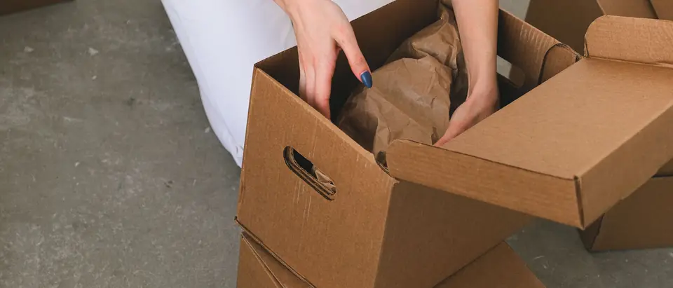 Hands packing paper-wrapped items into a cardboard box