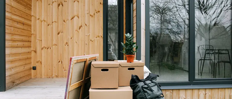 Lidded boxes, a backpack and a potted plant on a timber deck outside a house